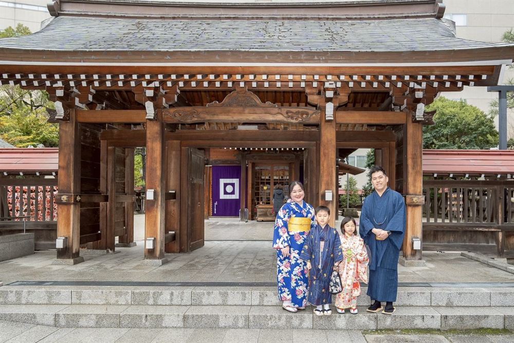 Family in kimono in front of a wooden shrine gate in central Fukuoka