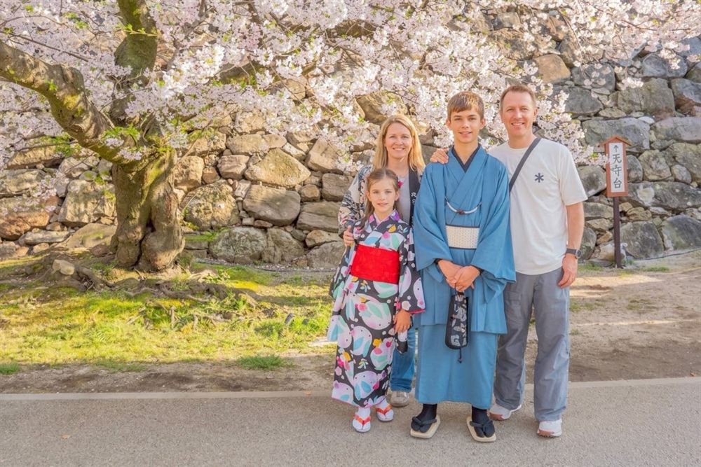 Family in kimono under cherry blossoms by the stone walls of Fukuoka Castle