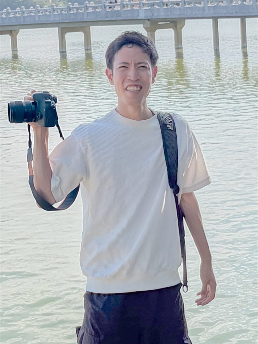 Mitch, the photographer, smiling with a camera by the lake at Ohori Park in Fukuoka